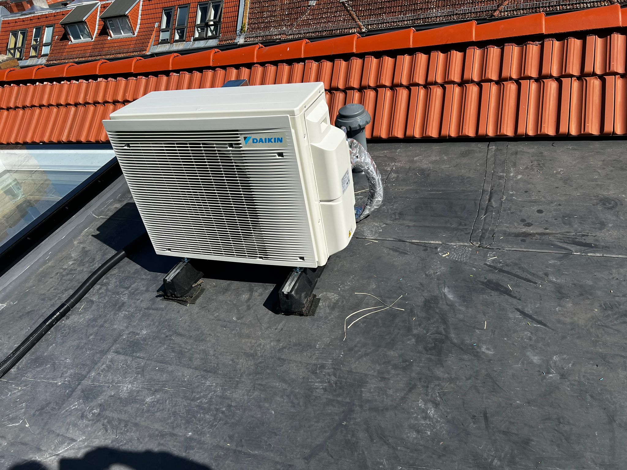 Daikin Außengerät auf Berliner Flachdach mit rotem Ziegeldach im Hintergrund – Anlagenbau